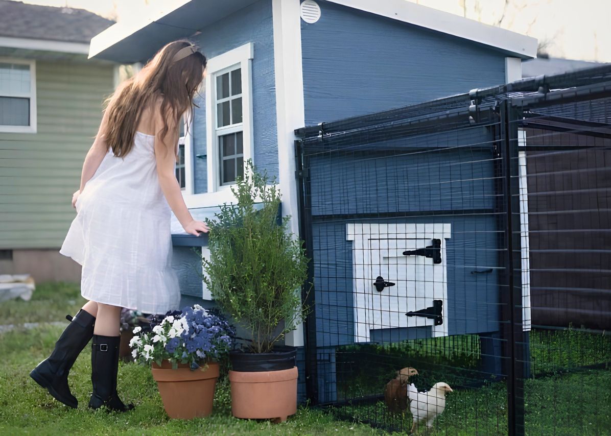 Girl by a blue large chicken coop with a run and potted flowers