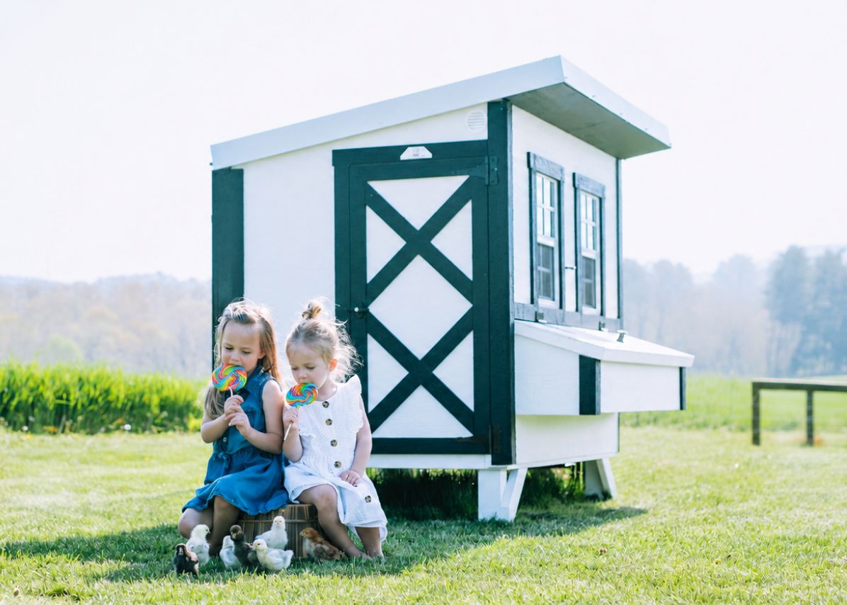 Two girls sitting by a white farmhouse-style large chicken coop